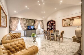 A spacious living room with a marble floor, a leather sofa, a dining area with chairs, a television, and a bookshelf. - CRISPI HOLIDAY IN (Roma)