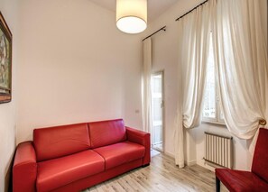 A room with a red sofa, a chair, a radiator, and a window with curtains. - CRISPI HOLIDAY IN (Roma)