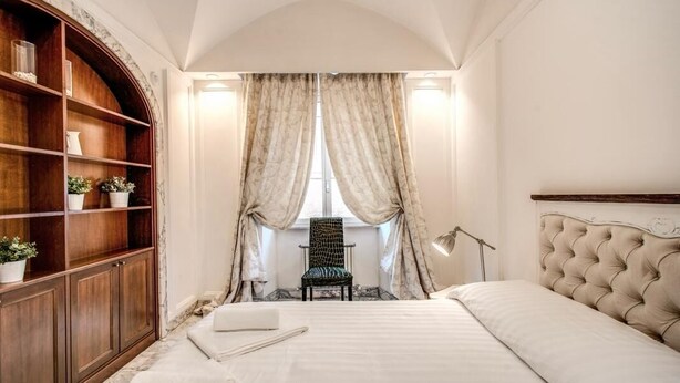 A bedroom with a bed, a chair, a bookshelf, and a window with curtains. - CRISPI HOLIDAY IN (Roma)