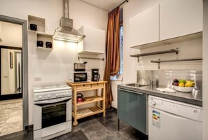 Eine kleine Küche mit Herd, Mikrowelle und Geschirrspüler, einem Holzregal und einem Fenster mit Vorhängen.