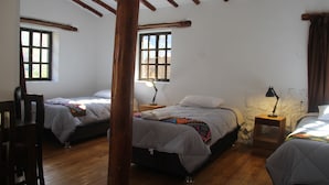 Quarto com duas camas, vigas de madeira no teto e parede de pedra.