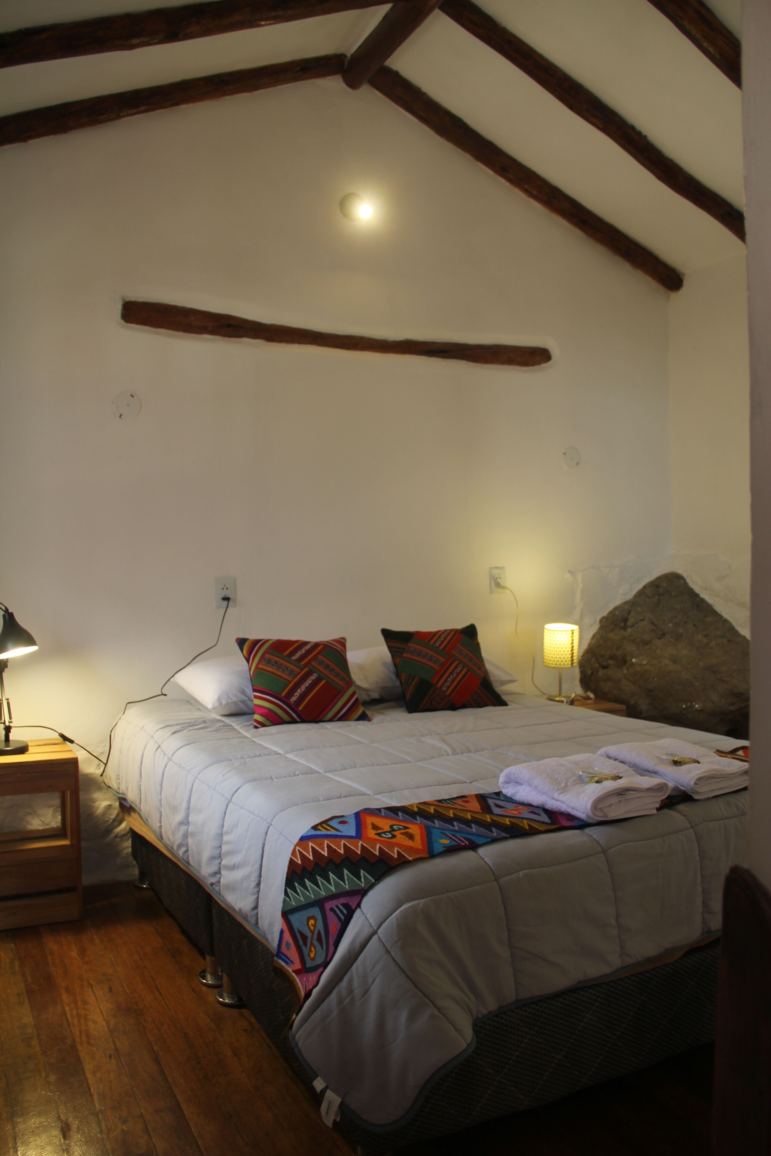 Ein Schlafzimmer mit einem Bett, Kissen, einem Nachttisch, einer Lampe und einer Wandleuchte.
