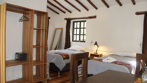 Quarto com duas camas, uma escrivaninha de madeira, uma cadeira, um espelho e uma janela com cortinas.