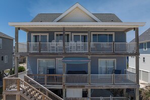 A two-story building with a balcony on the upper floor, a covered area with a sign, and a staircase leading to the entrance. - Oceanfront hot tub and elevator (North Topsail Beach)