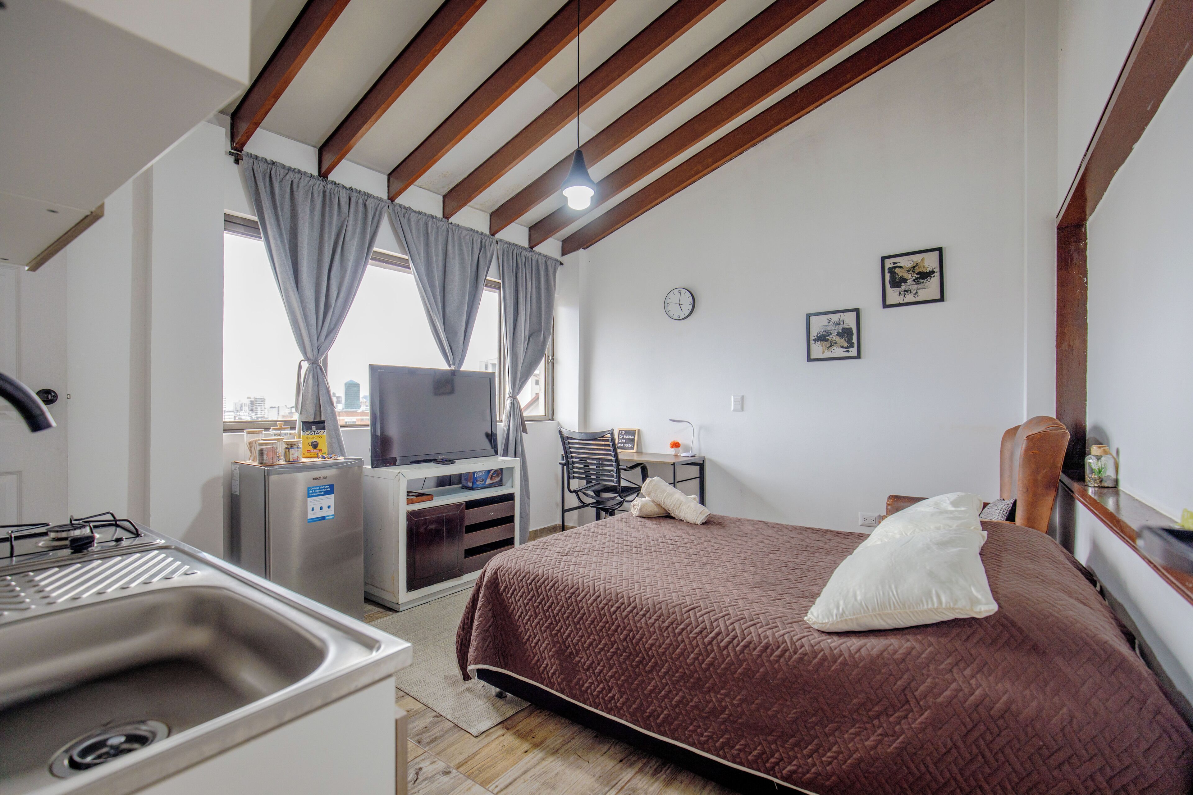 Une chambre d’hôtel avec un lit, une télévision, un bureau et une fenêtre avec des rideaux.