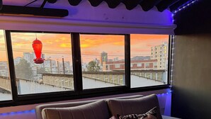 Sala de cinema com sofá, duas almofadas, controle remoto e vista para o pôr do sol.