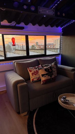 Une salle de cinéma avec un canapé, deux coussins, une télécommande et une vue sur un coucher de soleil.