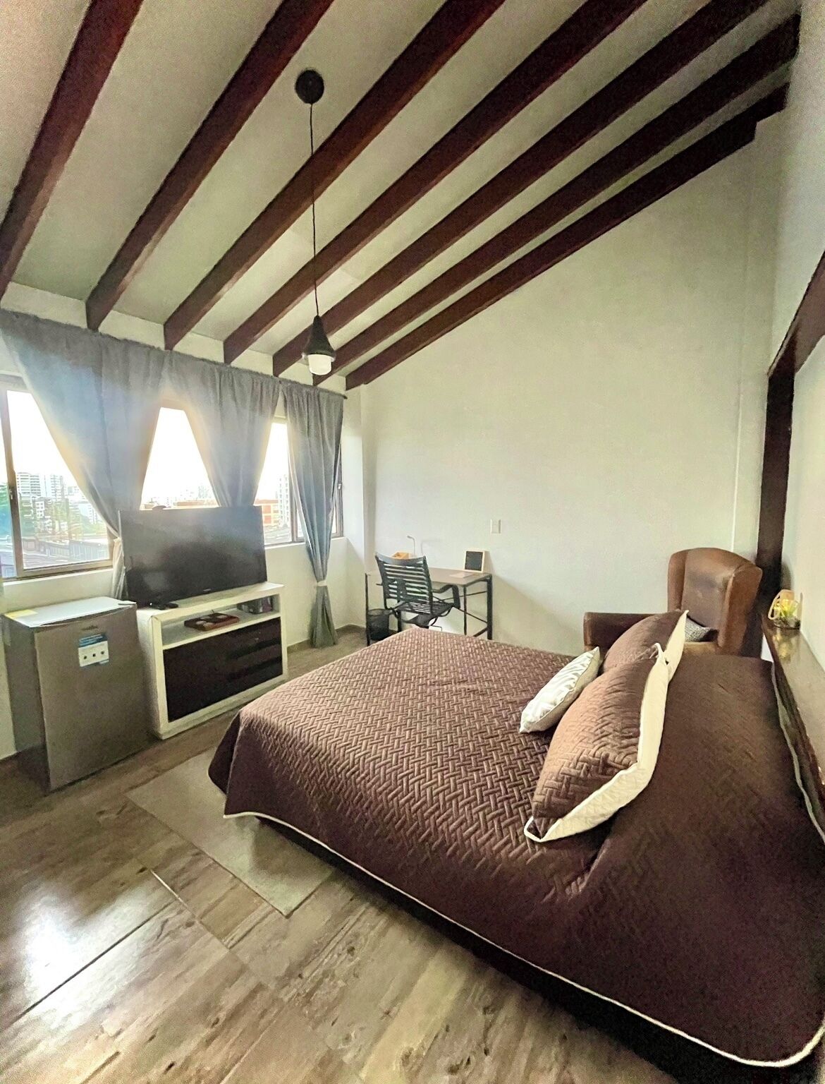 A bedroom with a bed, a desk, a chair, a television, and a window with curtains.