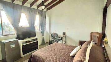 Un dormitorio con una cama, un escritorio, una silla, un televisor y una ventana con cortinas.