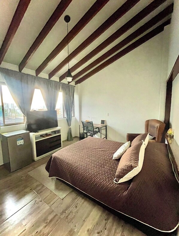 A bedroom with a bed, a desk, a chair, a television, and a window with curtains.