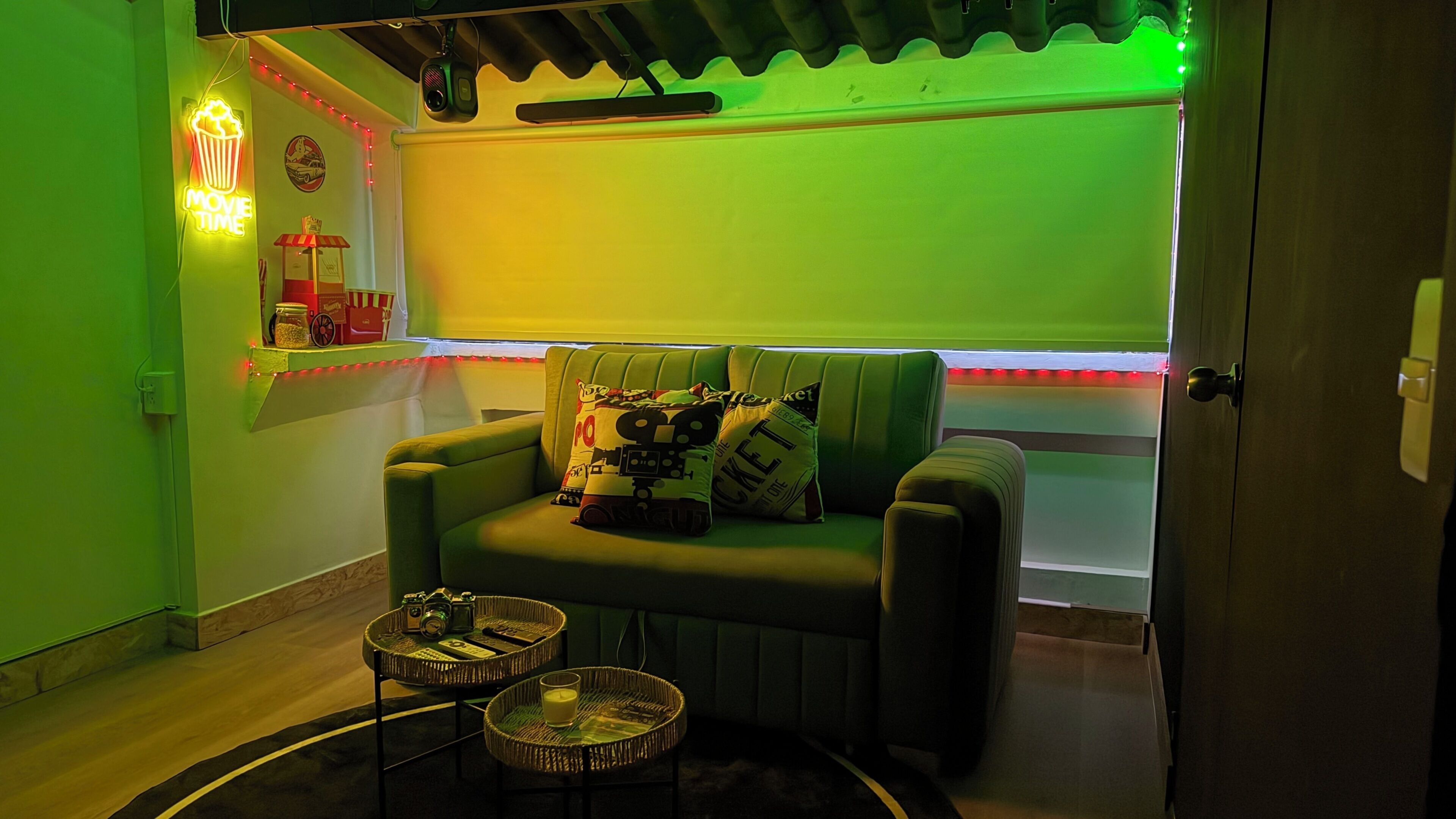 Um quarto aconchegante com um sofá verde, uma mesinha com câmeras e um letreiro neon.