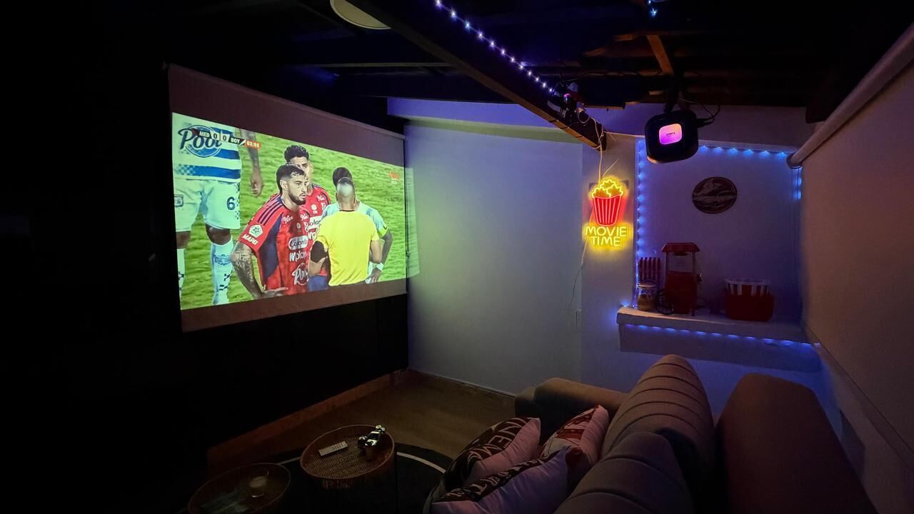 A cozy room with a large screen for watching sports, a comfortable couch, and a neon sign indicating a movie theater.