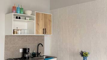 A compact kitchen with a gas stove, white cabinets, and a small dining table with a chair.