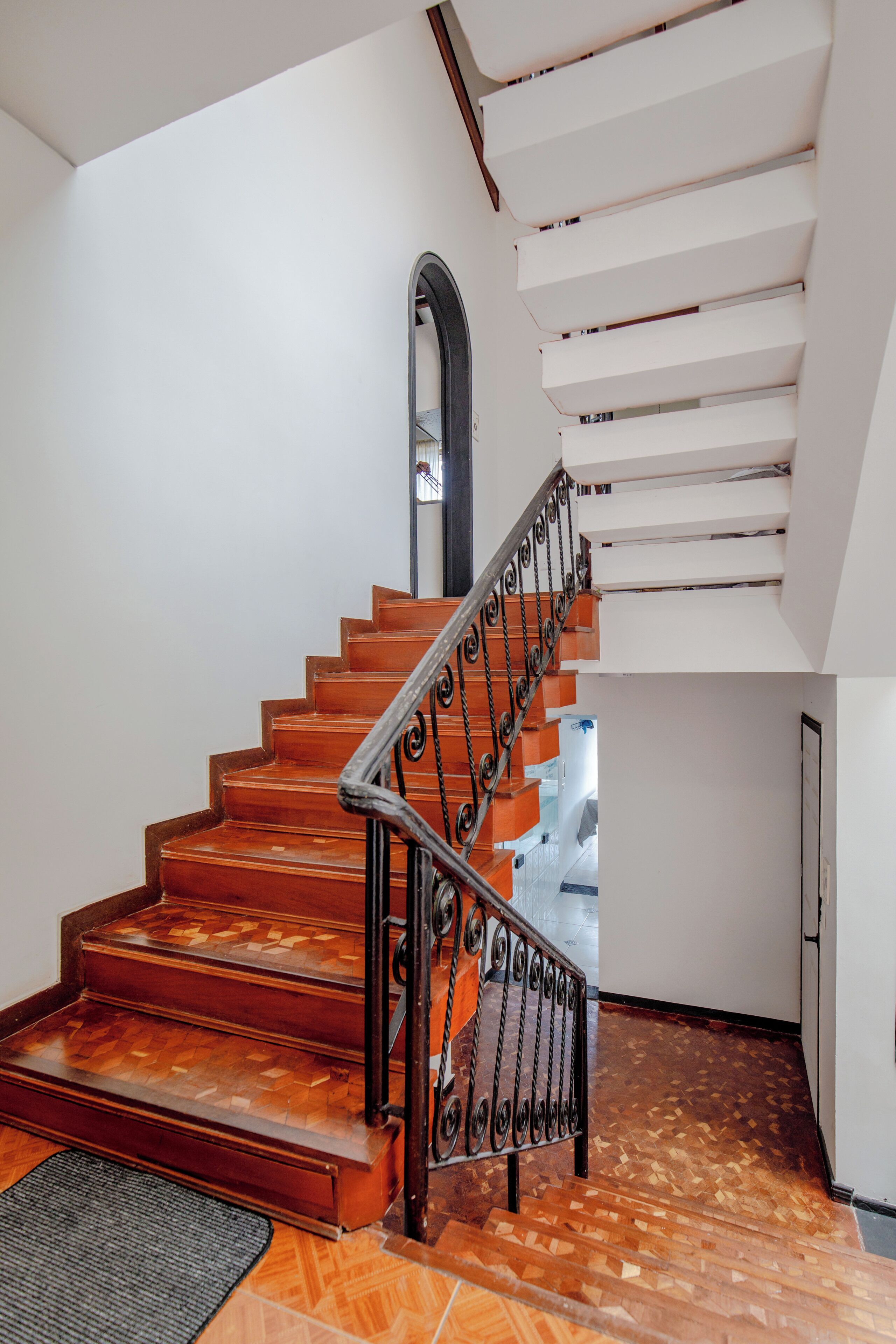 A staircase with wooden steps and a metal railing, leading to a landing with a white wall and a door.