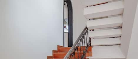 Escadaria com degraus de madeira e corrimão de metal, que leva a um patamar com parede branca e porta.