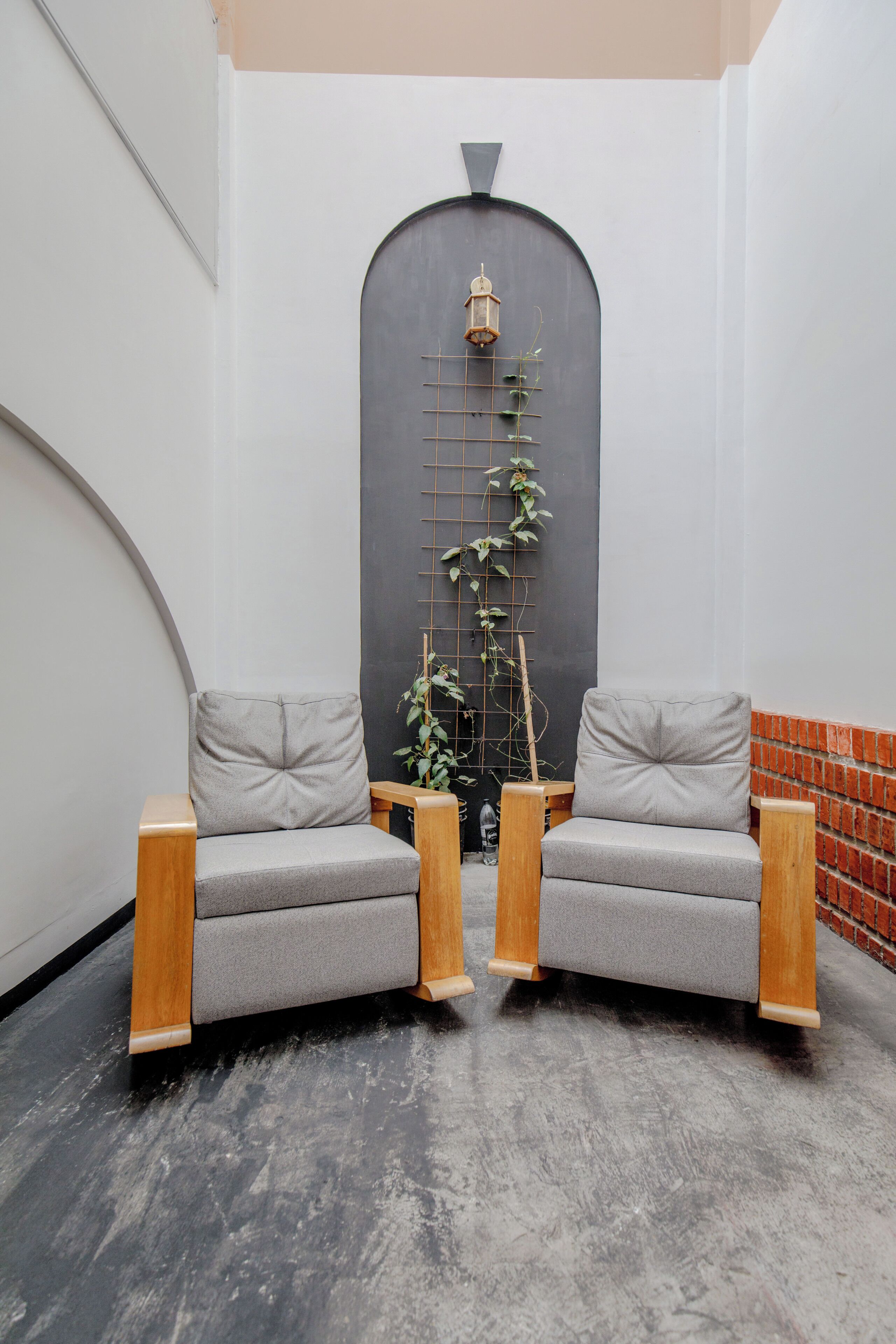 Un interior moderno con dos sofás grises, un banco de madera, piso de baldosas blanco y negro, pared de ladrillo y planta trepando una estructura de rejilla.