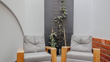 Un interior moderno con dos sofás grises, un banco de madera, piso de baldosas blanco y negro, pared de ladrillo y planta trepando una estructura de rejilla.