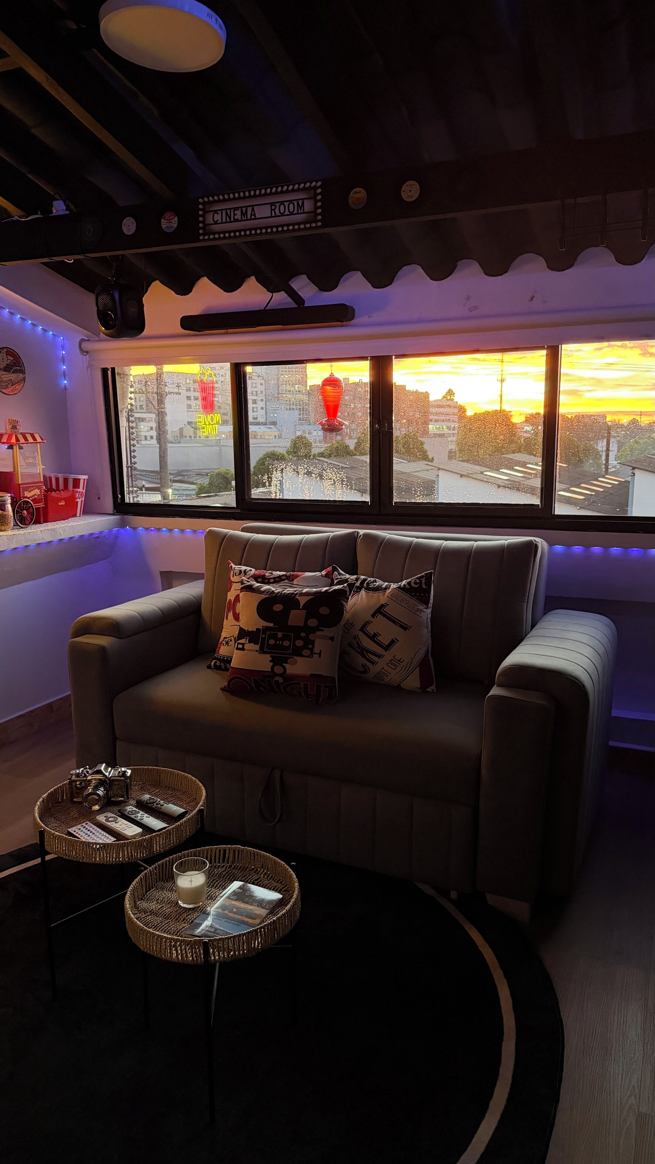 Una sala de cine con un sofá, dos mesitas auxiliares y un ventanal con vistas a la ciudad.