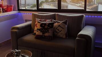 Una sala de cine con un sofá, dos mesitas auxiliares y un ventanal con vistas a la ciudad.