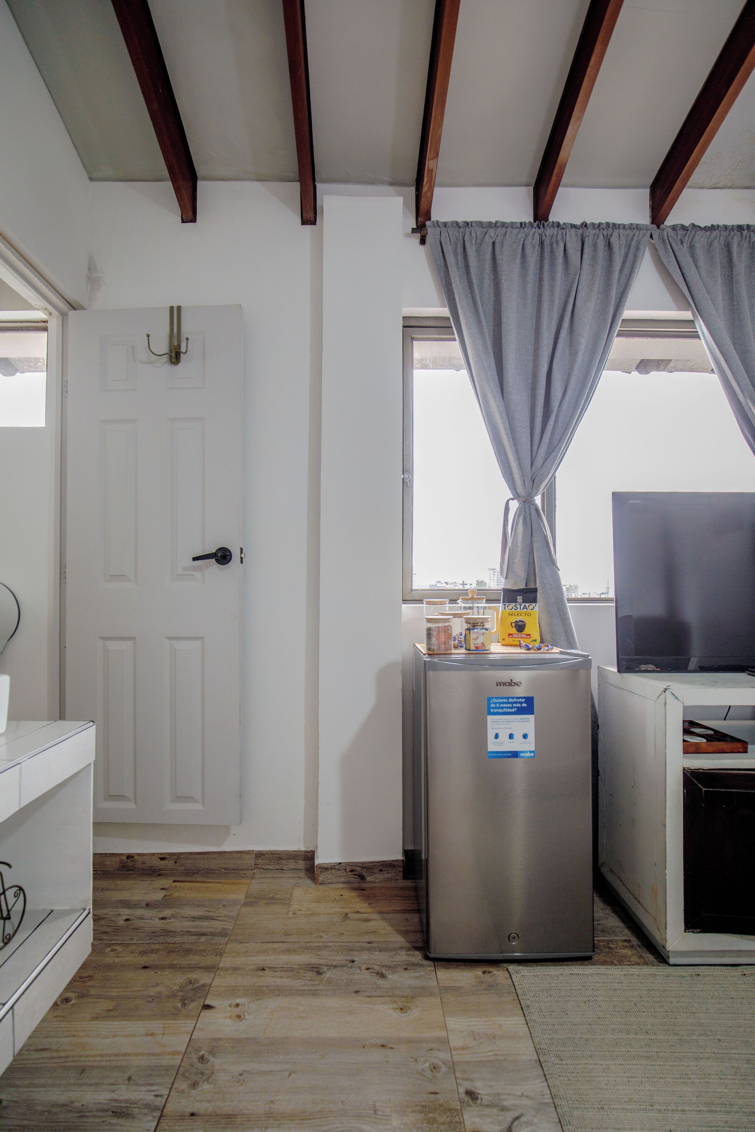 Una kitchenette equipada con refrigerador, cafetera y ventana con cortinas.
