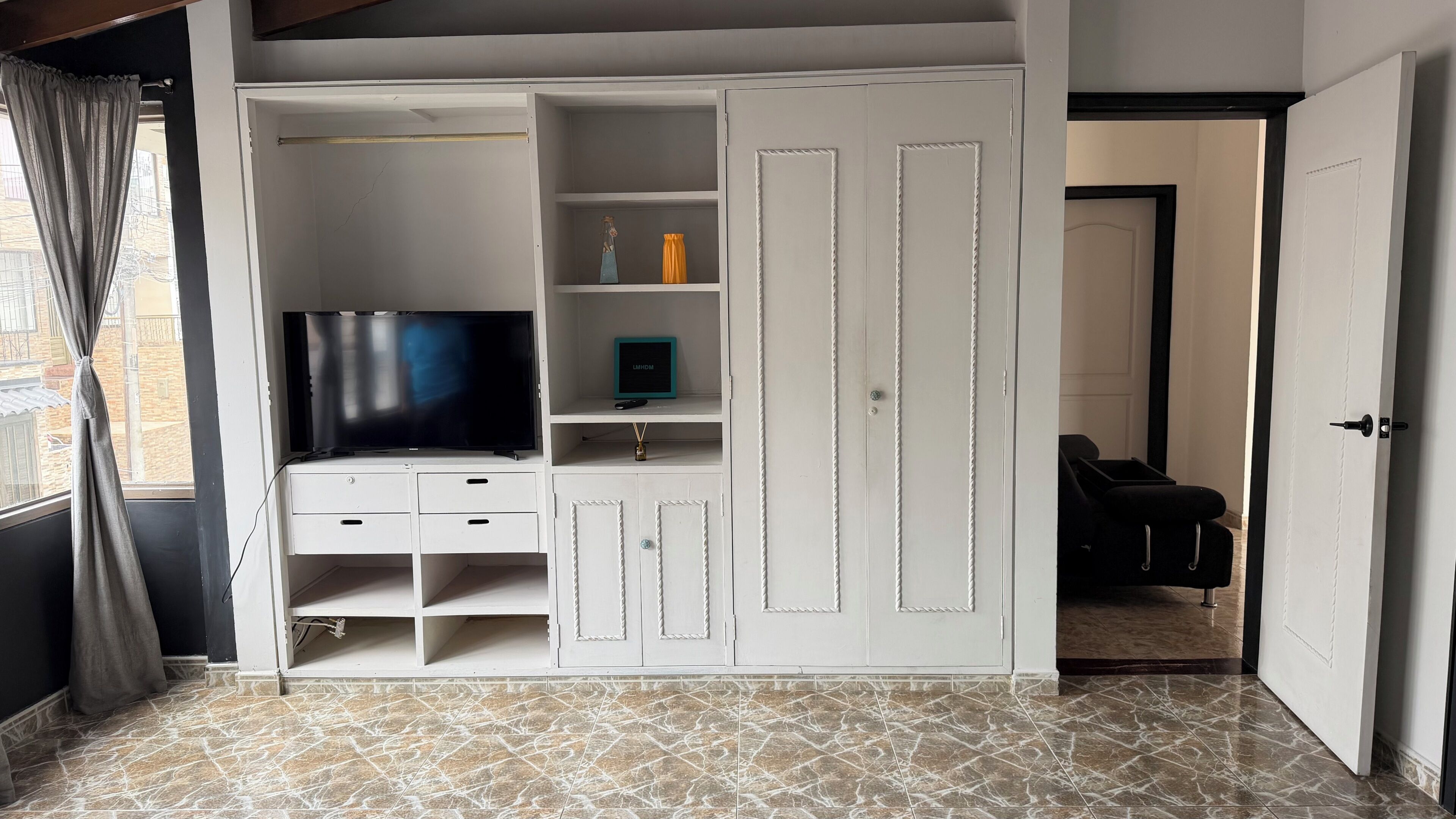 Een kamer met een televisie, lades, planken en een kledingkast.