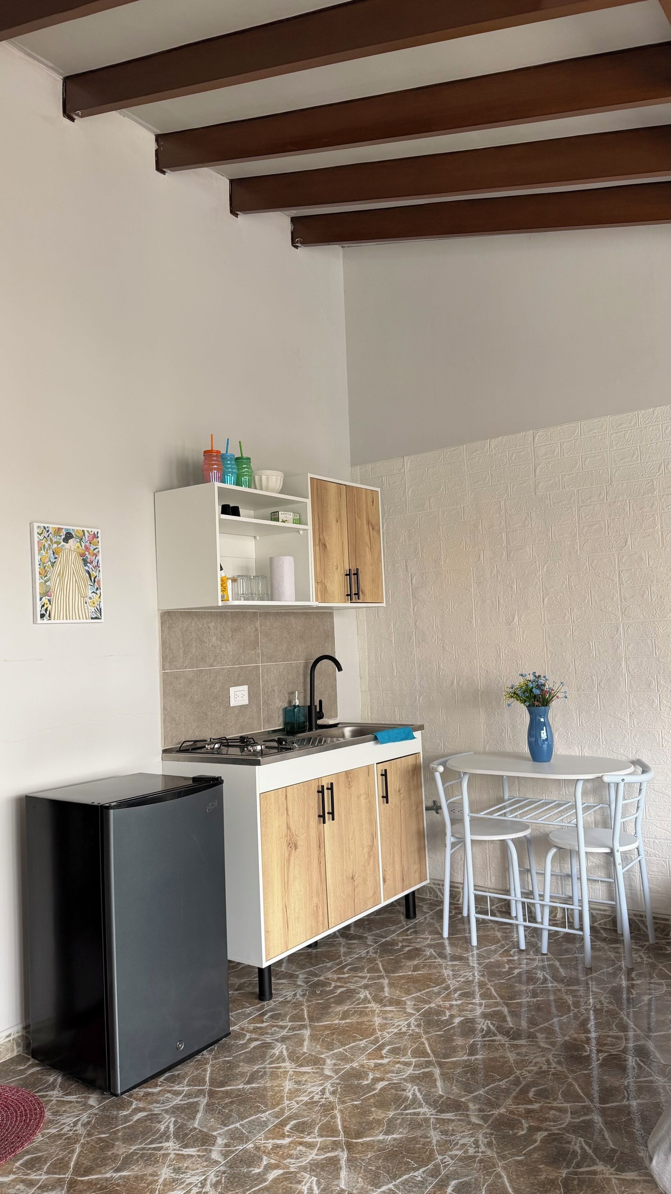 A compact kitchen with a refrigerator, wooden cabinets, a sink, and a dining area with a table and chairs.