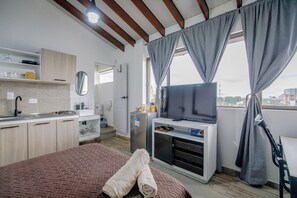 A compact hotel room with a kitchenette, a bed with a rolled-up blanket, a television, and a window with curtains. - Casa Sereno Manizales (Manizales)