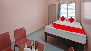 Una habitació d'hotel amb un llit, dues cadires, una taula i un bullidor, i un aparell d'aire condicionat.