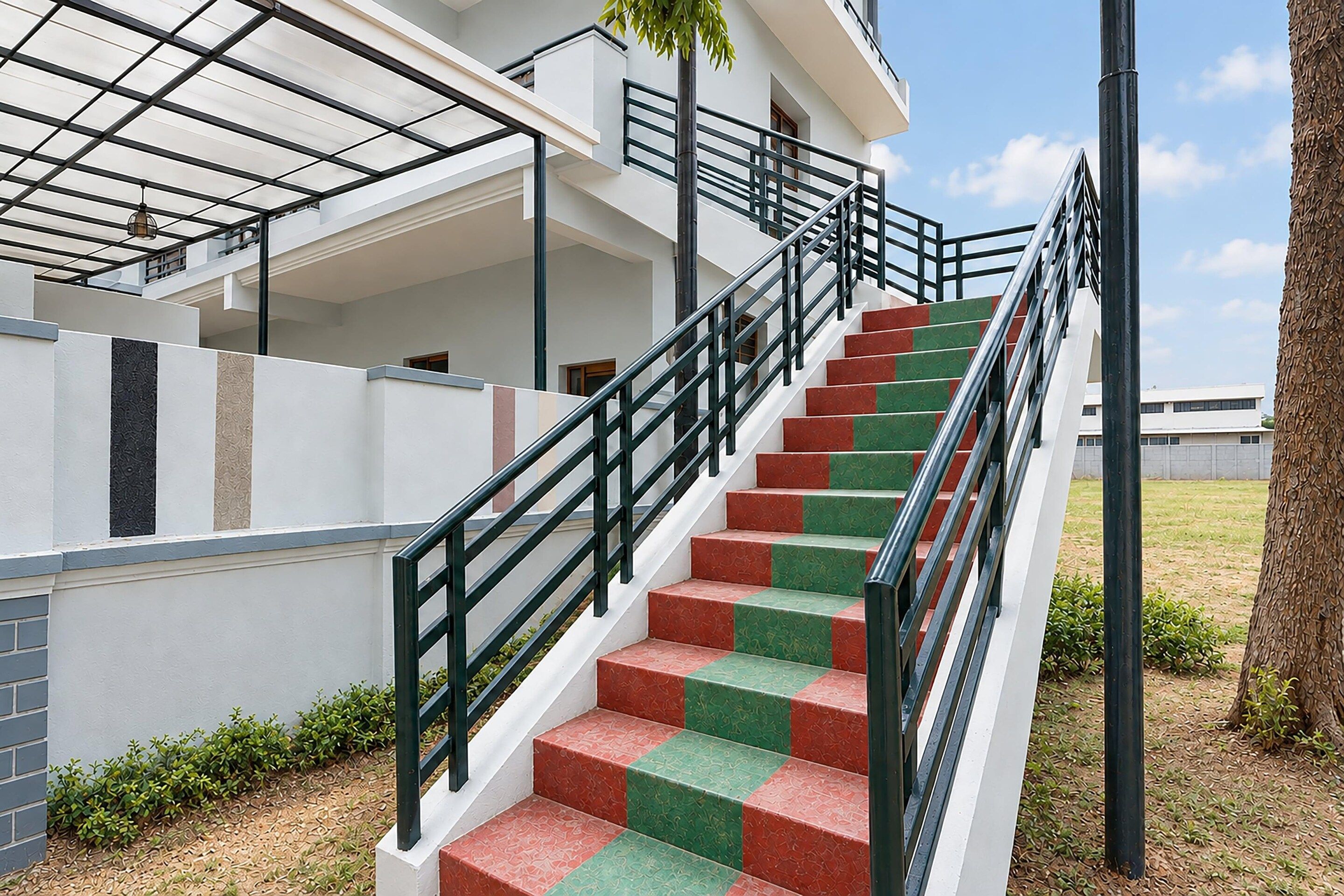 A staircase with alternating red and green steps leading to a white building with a black railing.