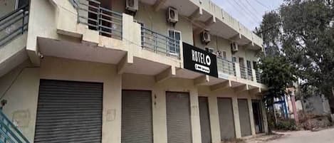 A hotel building with multiple balconies, air conditioning units, and closed shutters on the ground floor.