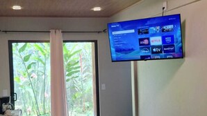 Una sala de estar moderna con un televisor de pantalla plana montado en la pared, un sofá, una mesa de centro y vistas a la vegetación a través del ventanal.