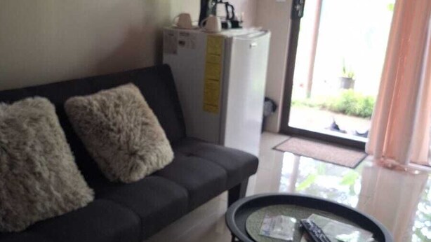 Una sala de estar con un sofá, una cafetera y una mesa de vidrio con mandos a distancia.