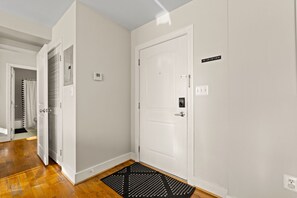 Un pasillo con una puerta blanca, un termostato y un felpudo negro.