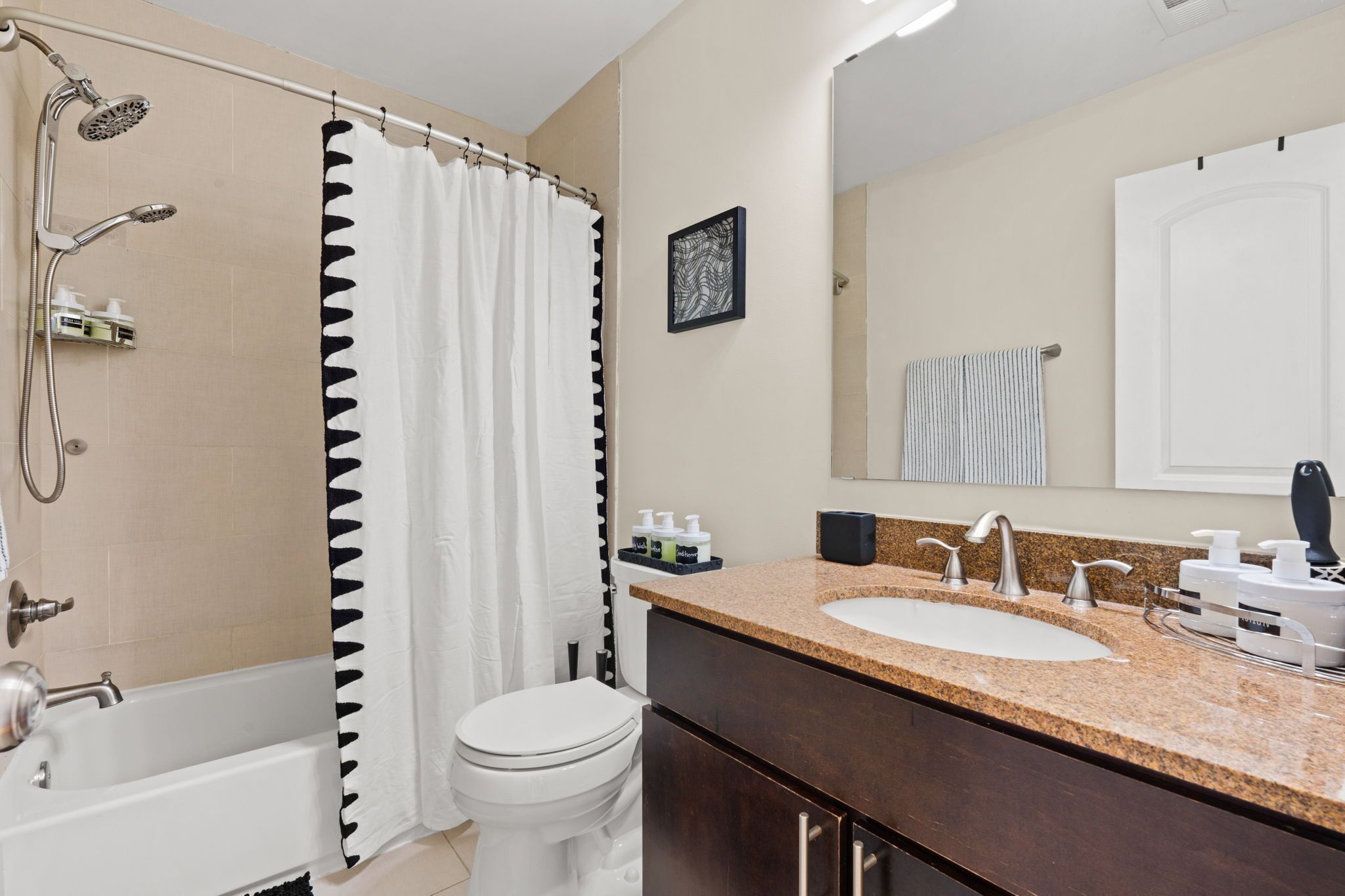Un baño con una bañera, ducha, inodoro, lavamanos con encimera de granito y espejo.