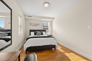 Un dormitorio con cama, mesita de noche, espejo y ventana.