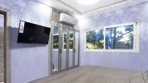 Un dormitorio con cama, televisor montado en la pared, ventana con vistas a árboles y puerta con paneles de vidrio.