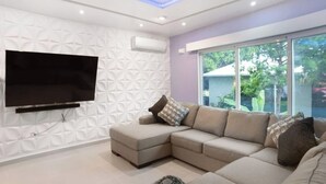 Una sala de estar moderna con un sofá modular, un televisor de pantalla plana montado en una pared con textura y un ventanal con vistas a zonas verdes.
