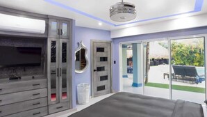 A bedroom with a large bed, a TV mounted on the wall, and a sliding glass door leading to a pool area.