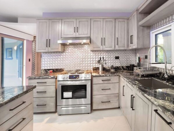 A modern kitchen with stainless steel appliances, light-colored cabinets, and a patterned backsplash.