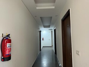 Un pasillo con extintor fijado en la pared, una puerta a la derecha e iluminación empotrada en el techo.