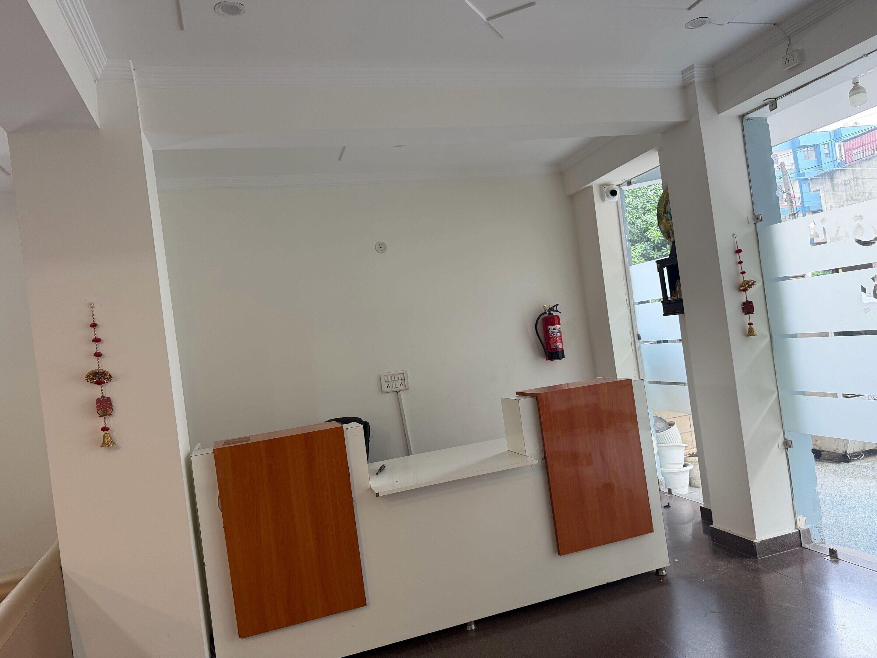 A reception desk with a white wall, a fire extinguisher mounted on the wall, and a door leading outside.