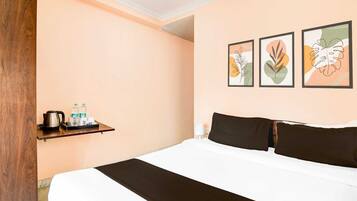 A hotel room with a bed, a shelf with toiletries, and three framed artworks on the wall.