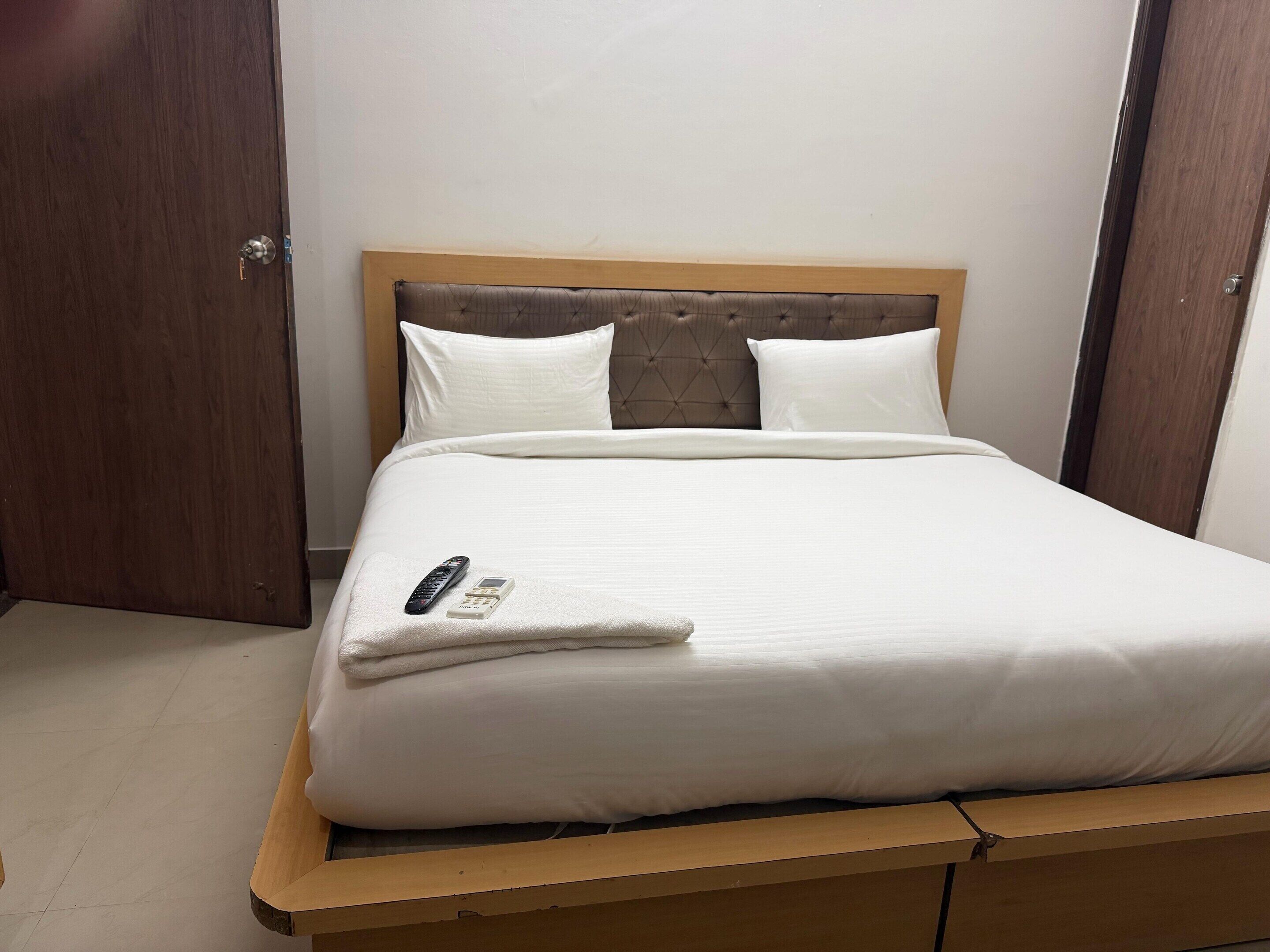 A neatly made bed with a wooden headboard, white bedding, and a remote control on the bed.