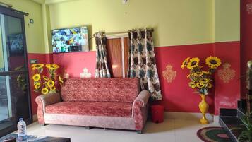 A living room with a sofa, a television mounted on the wall, and a red and yellow wall design.