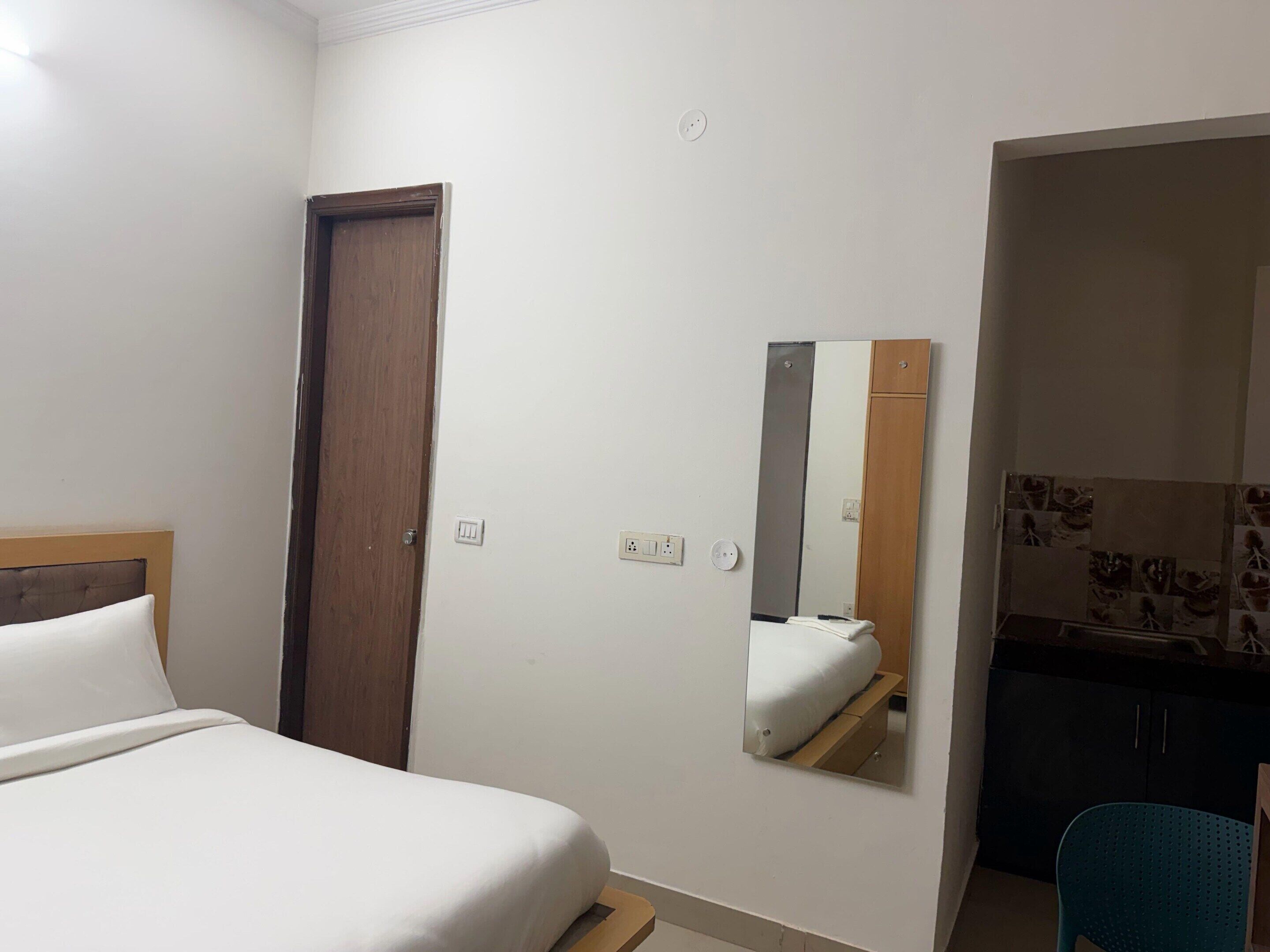 A hotel room with a bed, a wooden door, a mirror, and a kitchenette area.