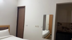 A hotel room with a bed, a wooden door, a mirror, and a kitchenette area.