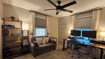 A home office with a desk, two monitors, a chair, a ceiling fan, and a bookshelf.