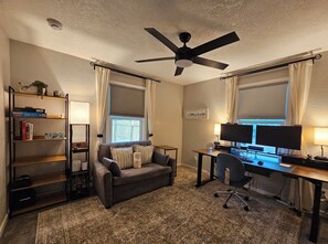 A home office with a desk, two monitors, a chair, a ceiling fan, and a bookshelf.