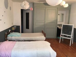Ein Zimmer mit zwei Einzelbetten, einem Holzschrank, einem Spiegel und einer auf einem Gestell stehenden Tafel.