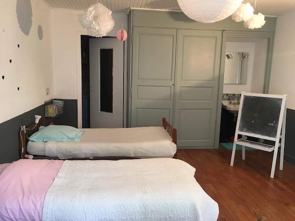 A room with two single beds, a wooden wardrobe, a mirror, and a whiteboard on a stand.